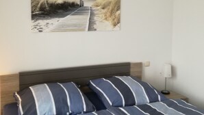 A bedroom with a bed, striped pillows, a headboard, and a wall-mounted picture of a beach path.