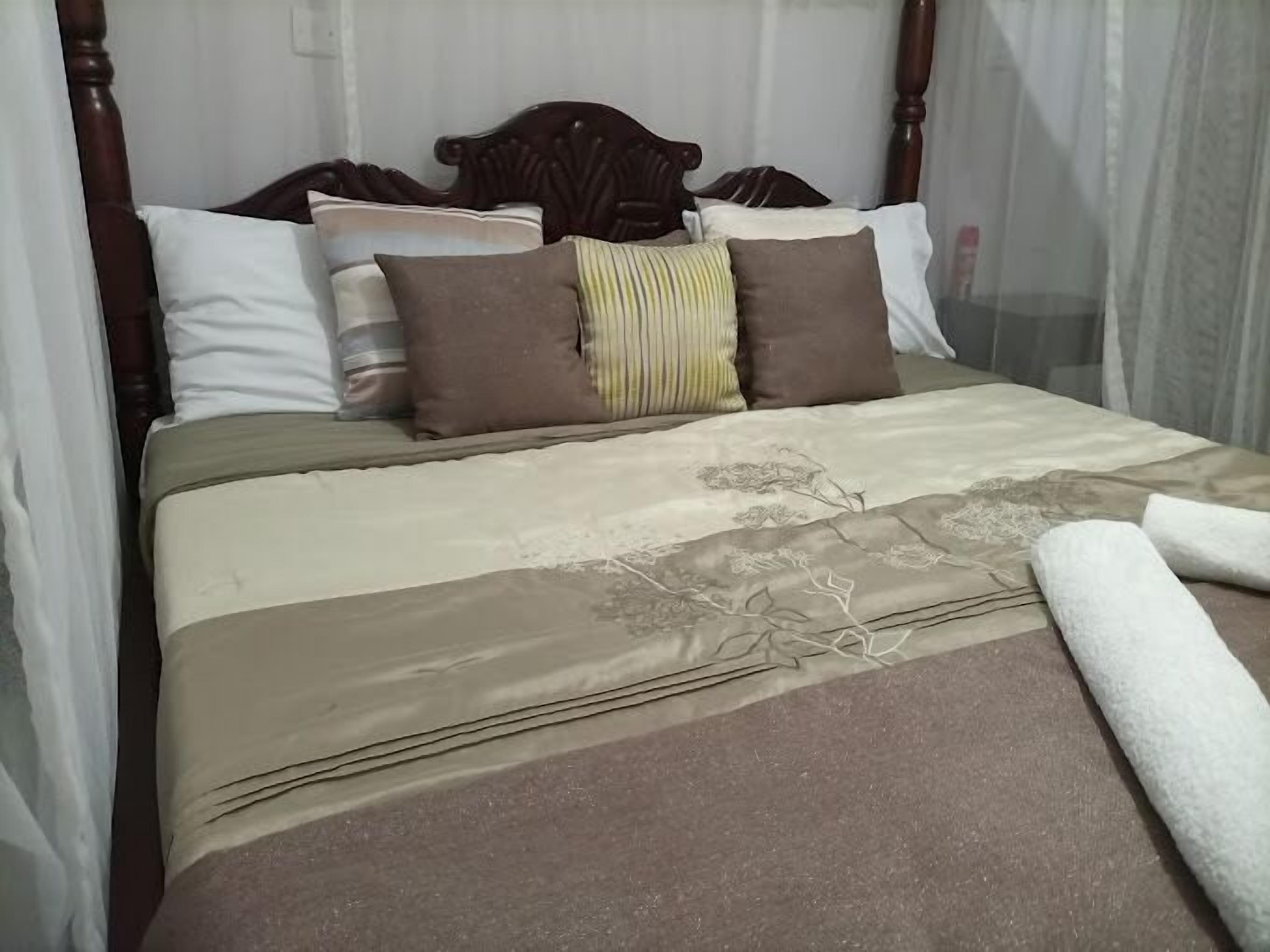 Una cama con dosel, varias almohadas y una colcha estampada con motivos florales.