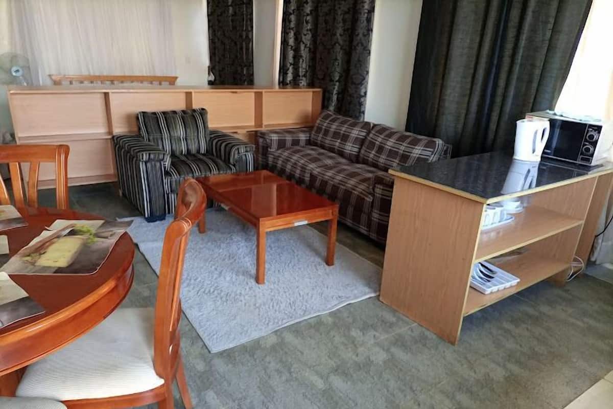 Un espacio habitable compacto con sofá, una mesa de centro, zona de comedor con sillas, pequeña cocina y ventana con cortinas.