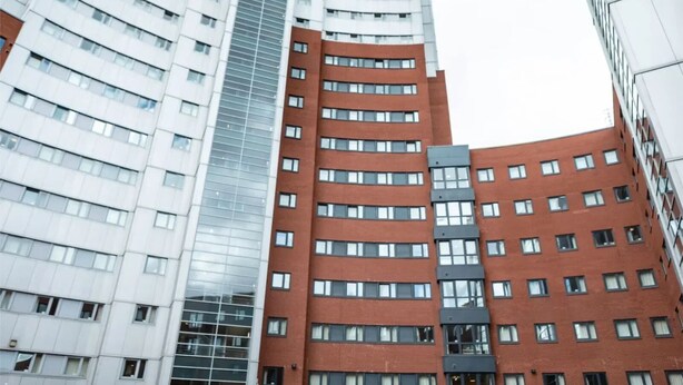 A modern high-rise building with a mix of glass and brick facades, featuring multiple floors and a prominent central elevator shaft. - Belgrave View - Campus Accommodation (Birmingham)