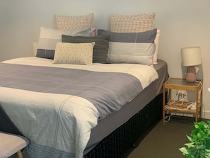 A neatly made bed with a grey and white duvet, a bedside table with a lamp, and a plant on the floor. - Beautiful and Convenient apartment in CBD (Melbourne)