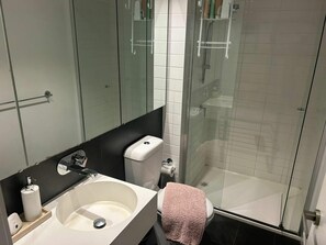 A modern bathroom with a glass shower enclosure, a white sink, and a toilet. - Beautiful and Convenient apartment in CBD (Melbourne)