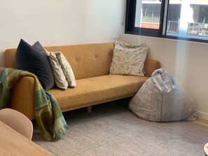 Una habitación con sofá, almohadas, una manta y un sillón de peluche.