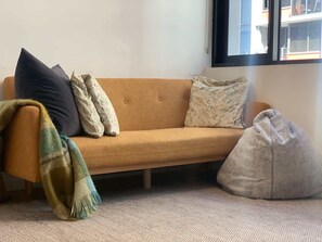 Ein Sofa mit mehreren Kissen, einer Decke und einem Sitzsack in einem Raum mit einem Fenster.