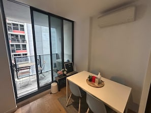 A modern room with a large sliding glass door leading to a balcony, a small table with a plant, and a chair. - Beautiful and Convenient apartment in CBD (Melbourne)