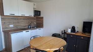A compact kitchen with a wooden table and chairs, a microwave, a coffee maker, and a TV. - Charming studio cabin in the heart of Font Romeu (font romeu)