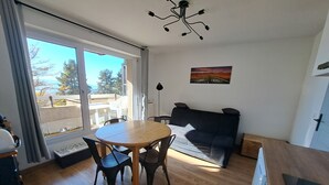 A living room with a wooden dining table, black chairs, a black sofa, and a ceiling light fixture. - Charming studio cabin in the heart of Font Romeu (font romeu)