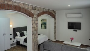 A hotel room with a bed, a sofa, a TV, and a stone archway. - Oliva Mare (Turunc)