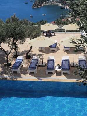 A poolside area with lounge chairs and umbrellas, overlooking a body of water with boats. - Oliva Mare (Turunc)