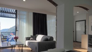 A modern hotel room with a bed, a sofa, a dining table with flowers, and a view of the mountains. - Oliva Mare (Turunc)