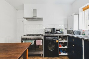 A compact kitchen with a stove, oven, and washing machine. - Rustic 2-Bed Home + Garden (Greater London)