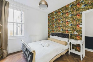 Ein Schlafzimmer mit Bett, Nachttisch, Lampe, Heizkörper und einem Fenster mit Vorhängen.