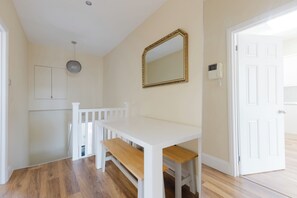 Una habitación con una mesa blanca y un banco, un espejo con marco dorado y una puerta blanca.