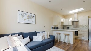 Ein modernes Wohnzimmer mit einem blauen Sofa, einem Wandbild einer Weltkarte und einer Küchenzeile mit weißen Schränken und einem Edelstahlkühlschrank.