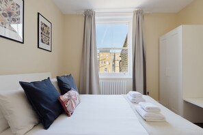 Une chambre d’hôtel avec un lit, des oreillers, une fenêtre avec des rideaux, un radiateur et une vue sur les bâtiments environnants.
