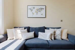 Una habitació amb un sofà blau, almoinades blanques i amb dibuixos, i una obra d'art amb un mapa del món a la paret.