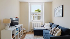 Ein Wohnzimmer mit einer Couch, einem Fernseher, einer Heizung und einem Fenster mit Blick auf ein Gebäude.