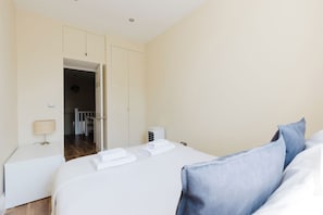 A hotel room with a bed, a nightstand, a lamp, and a door leading to a hallway.