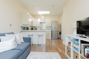A compact living space with a kitchenette, a sofa, a TV, and a bookshelf.