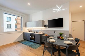 A modern kitchen with a built-in oven, a dining area with a table set for four, and a flat-screen TV mounted on the wall. - Central Apartment Piazza Dante Genova (Genoa)