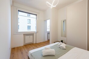 Een moderne slaapkamer met een groot bed, een raam, een radiator en een spiegel.
