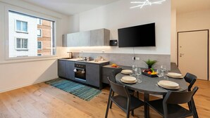 A modern kitchen with a built-in oven, a dining area with a table set for four, and a flat-screen TV mounted on the wall. - Central Apartment Piazza Dante Genova (Genoa)