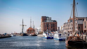 Un puerto con barcos amarrados, un barco de gran tamaño y edificios al fondo.
