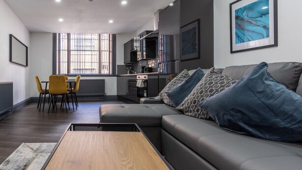 A modern living room with a sofa, a coffee table, and a dining area with chairs. - Temple Court by UStay Aparthotels (Liverpool)