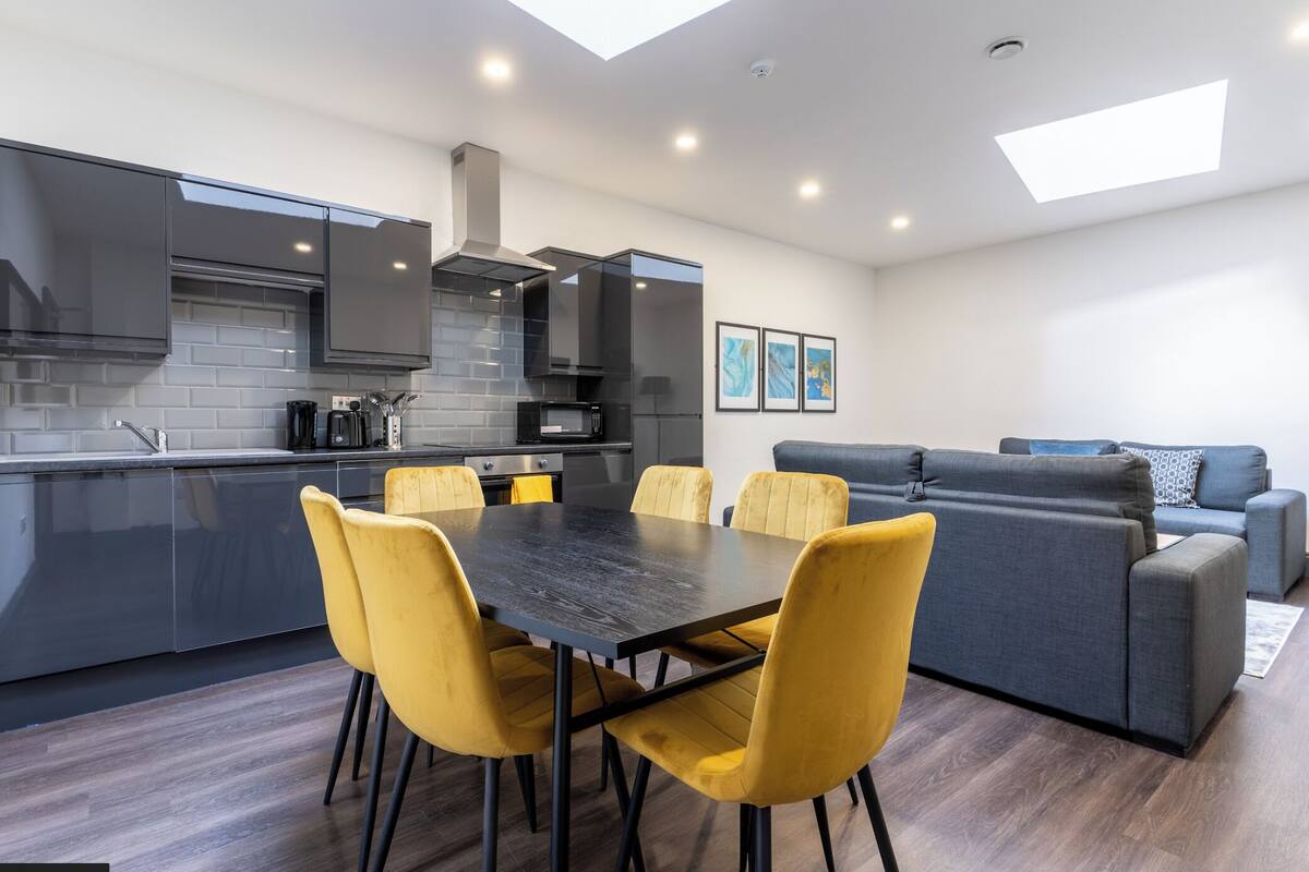 A modern kitchen with a dining area, built-in appliances, and a gray sofa in a living space.