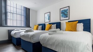 A hotel room with two beds, each with white bedding and blue headboards. There are two framed pictures on the wall, and a window with blinds. - Temple Court by UStay Aparthotels (Liverpool)
