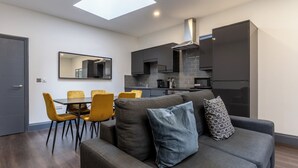 A modern living space with a sofa, dining table, and chairs, a kitchen area, and a skylight. - Temple Court by UStay Aparthotels (Liverpool)