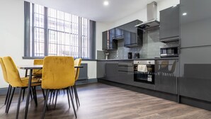 A modern kitchen with grey cabinets, a built-in oven, and a dining area with yellow chairs. - Temple Court by UStay Aparthotels (Liverpool)