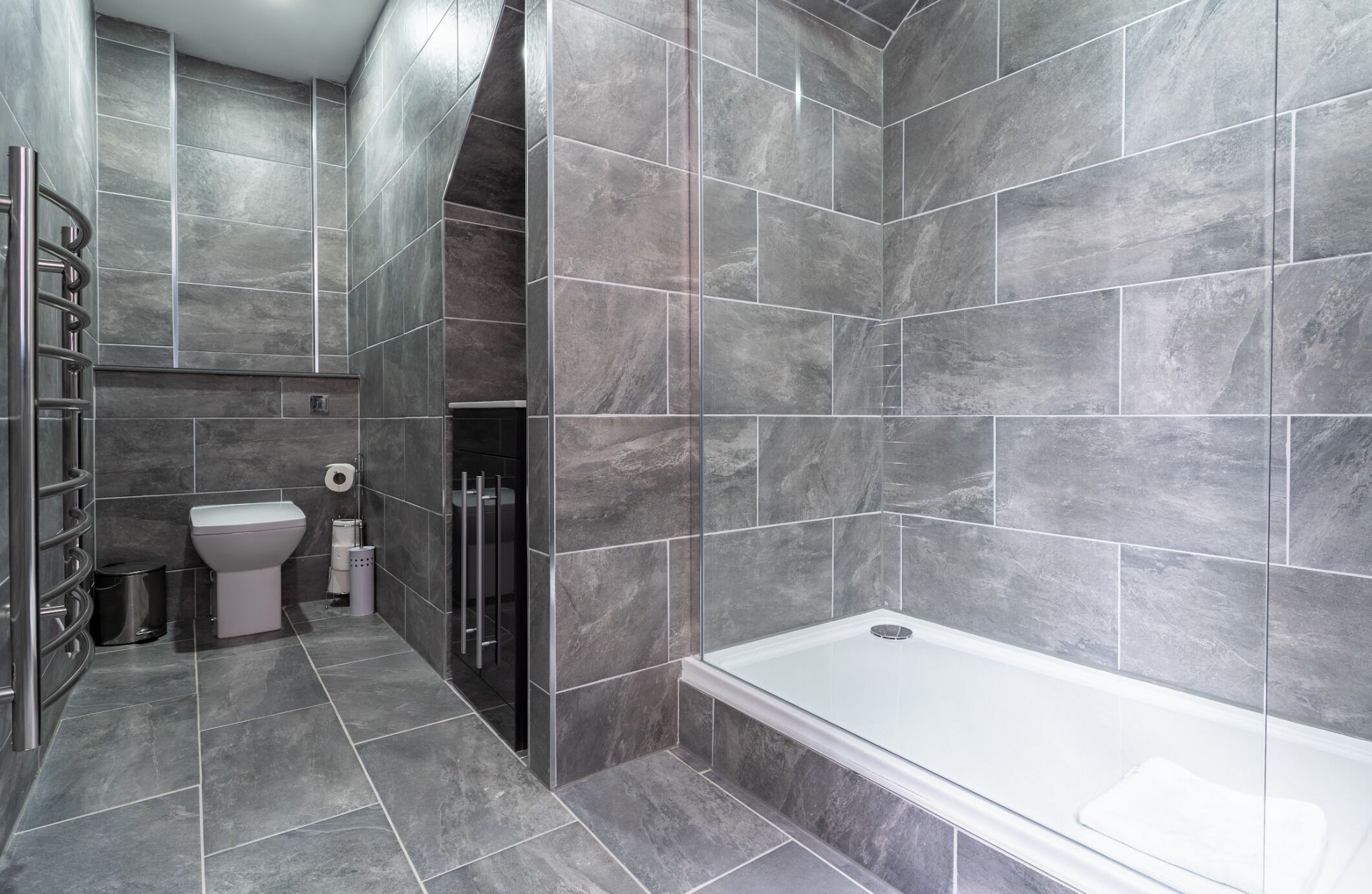 Une salle de bain moderne avec des carreaux gris, des toilettes, une douche et une baignoire.