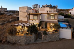 A modern multi-story house with a stone facade, a covered outdoor seating area, and a swimming pool. - Bougan Villa (Rhodes)