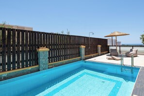 A swimming pool with a wooden fence, stone pillars, and lounge chairs with umbrellas. - Bougan Villa (Rhodes)
