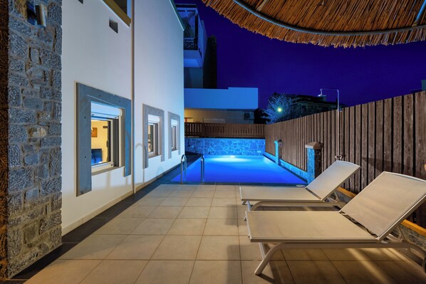 An outdoor swimming pool area with lounge chairs, a stone wall, and a wooden fence. - Bougan Villa (Rhodes)