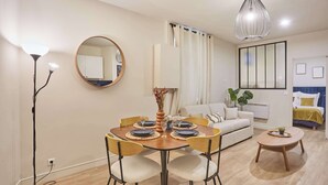 Un salón moderno con una mesa de comedor, sillas, un sofá, una mesa de centro, una lámpara de pie, una lámpara colgante, un espejo y una cortina.