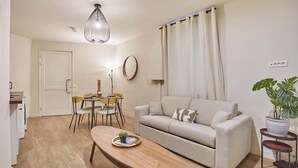 Una sala de estar moderna con un sofá, una mesa de comedor con sillas, una lámpara colgante y una planta en maceta.