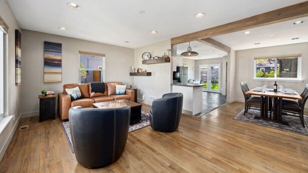 A spacious living room with a leather sofa, a dining area with a wooden table, and a kitchen in the background. - Magnolia Hideaway - Pet Friendly w/ Fireplace (Fort Collins)