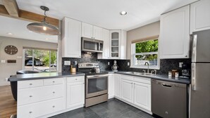 A modern kitchen with white cabinetry, stainless steel appliances, and a black tiled backsplash. - Magnolia Hideaway - Pet Friendly w/ Fireplace (Fort Collins)