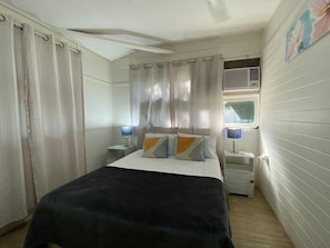 Un dormitorio con cama, dos mesitas de noche con lámparas, una ventana con cortinas y un radiador.