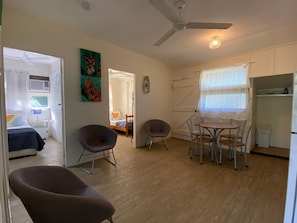 Un espacio habitable compacto con comedor, cama, ventilador de techo y ventana con cortinas ligeras.