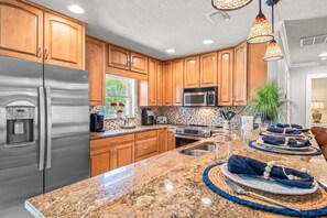 A kitchen with wooden cabinets, stainless steel appliances, granite countertops, and a dining area with a table set for two.