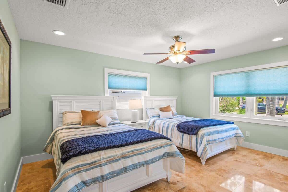A bedroom with two beds, a ceiling fan, a window with blinds, and a view of the outdoors.