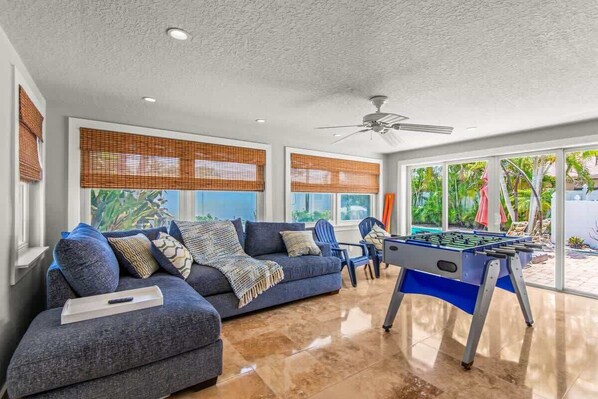 A living room with a sofa, a foosball table, and a ceiling fan.