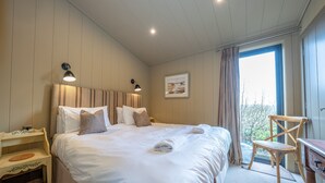 Una cama bien hecha con almohadas, una mesita de noche, una silla y una ventana con cortinas.