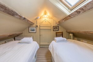 A bedroom with two beds, a skylight, a radiator, and a door. - Bryn-Chwilog | Traditional Welsh Stone Cottage On The Llyn Peninsula (Nr Aberdaron)