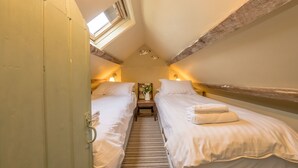 A room with two beds, a skylight, and a small table with a vase.