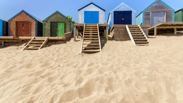 A row of beach huts with wooden staircases leading up to them.