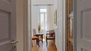 Un couloir avec un plancher en bois, une table à manger avec des chaises et une fenêtre avec des rideaux.